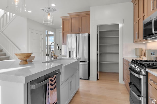kitchen with stainless steel appliances, a sink, recessed lighting, light wood-type flooring, and decorative light fixtures