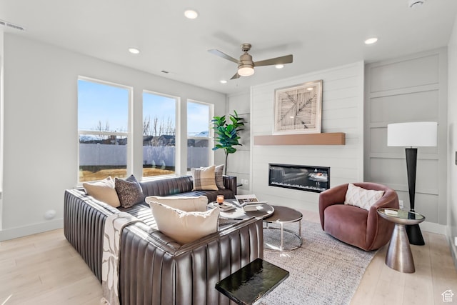living area featuring a ceiling fan, wood finished floors, a glass covered fireplace, baseboards, and recessed lighting