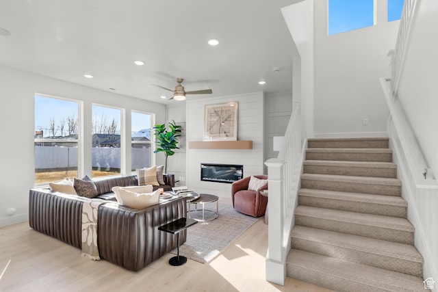 living area with stairs, wood finished floors, recessed lighting, a ceiling fan, and a glass covered fireplace