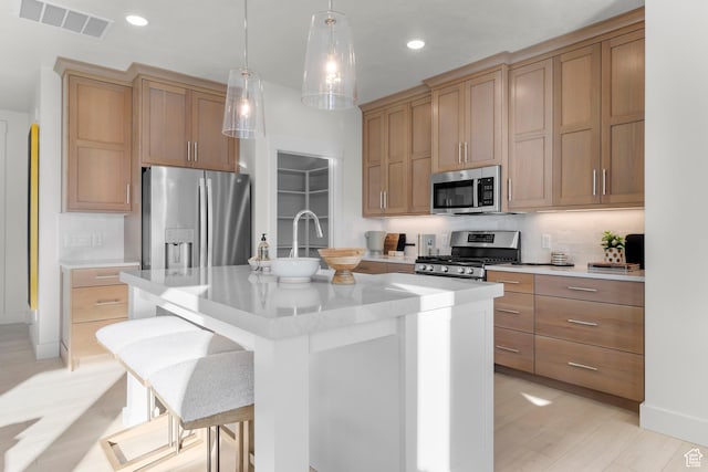 kitchen featuring appliances with stainless steel finishes, light countertops, an island with sink, recessed lighting, and hanging light fixtures