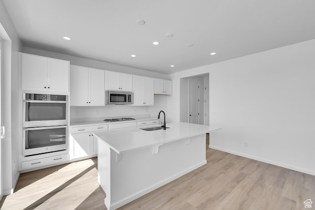 kitchen with stainless steel appliances, a sink, white cabinetry, light wood-style floors, and recessed lighting