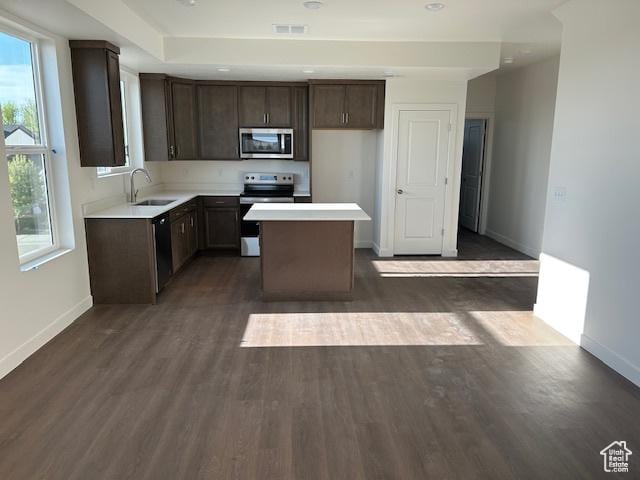 kitchen featuring stainless steel appliances, baseboards, a center island, a sink, and dark brown cabinets