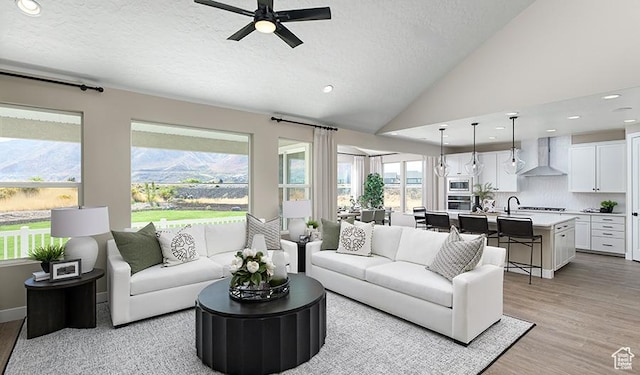 living room with a ceiling fan, light wood-type flooring, a textured ceiling, recessed lighting, and lofted ceiling