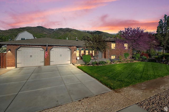 view of front facade with a mountain view, an attached garage, driveway, a lawn, and brick siding