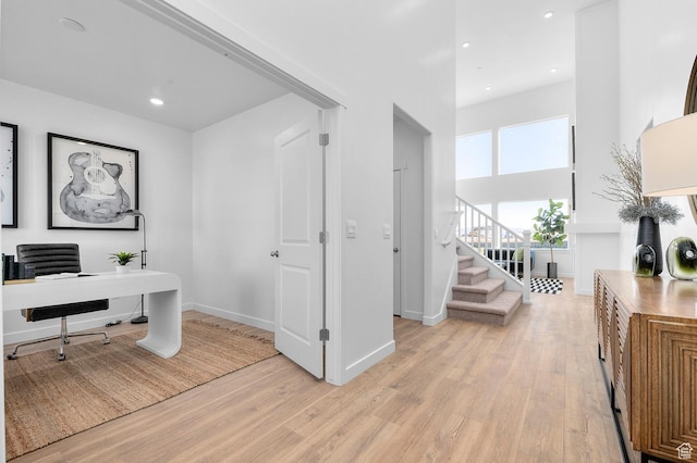 home office featuring light wood-type flooring, baseboards, recessed lighting, and a towering ceiling