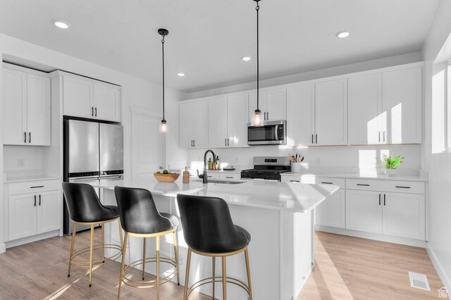 kitchen with stainless steel appliances, a sink, white cabinetry, light wood-style flooring, and an island with sink