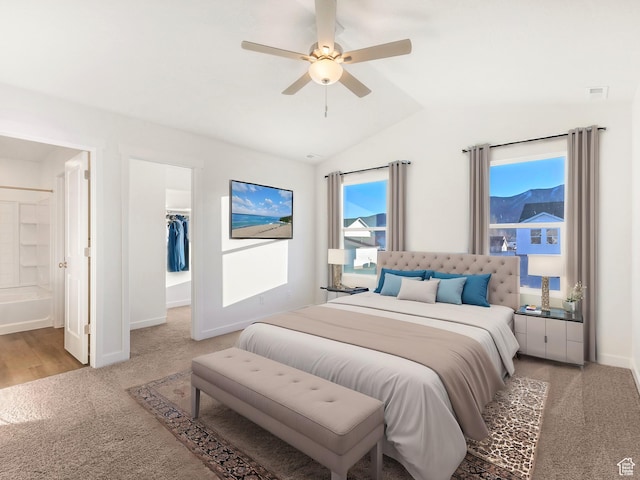 bedroom with light colored carpet, lofted ceiling, a walk in closet, ensuite bath, and baseboards