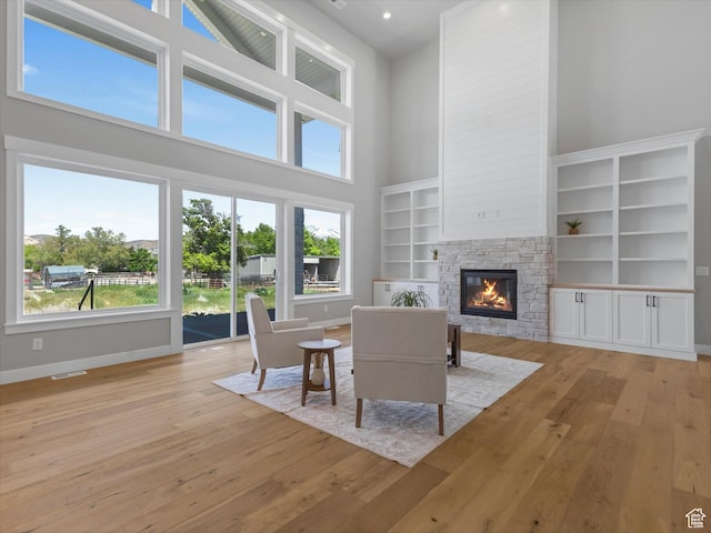 living area with a towering ceiling, a stone fireplace, light wood finished floors, baseboards, and recessed lighting