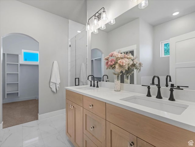 bathroom featuring double vanity, marble look tile flooring, a shower with shower door, baseboards, and a walk in closet