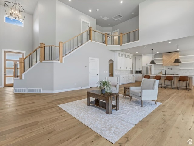 living area featuring a towering ceiling, light wood-type flooring, stairway, a chandelier, and baseboards