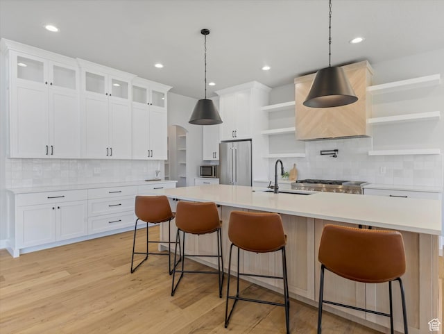 kitchen featuring open shelves, stainless steel appliances, a sink, an island with sink, and tasteful backsplash