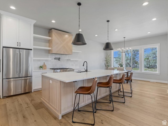 kitchen featuring high end fridge, a sink, open shelves, light countertops, and tasteful backsplash