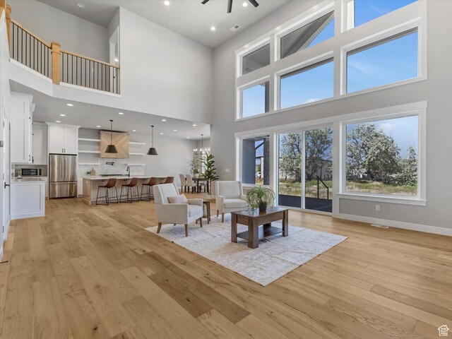 living area with a high ceiling, light wood-style flooring, ceiling fan, baseboards, and recessed lighting