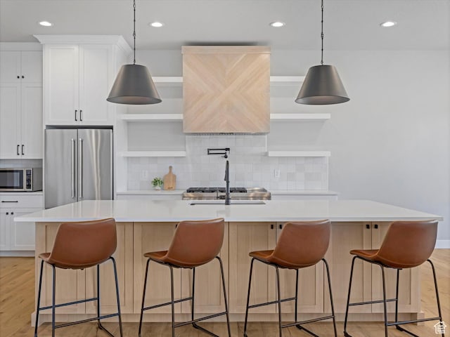 kitchen with stainless steel appliances, a center island with sink, light countertops, tasteful backsplash, and light wood-type flooring
