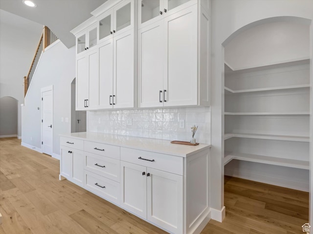 kitchen featuring arched walkways, light wood-style flooring, light countertops, white cabinetry, and backsplash