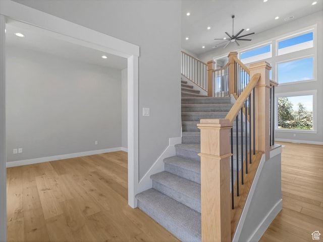 stairway with wood finished floors, recessed lighting, baseboards, and a towering ceiling