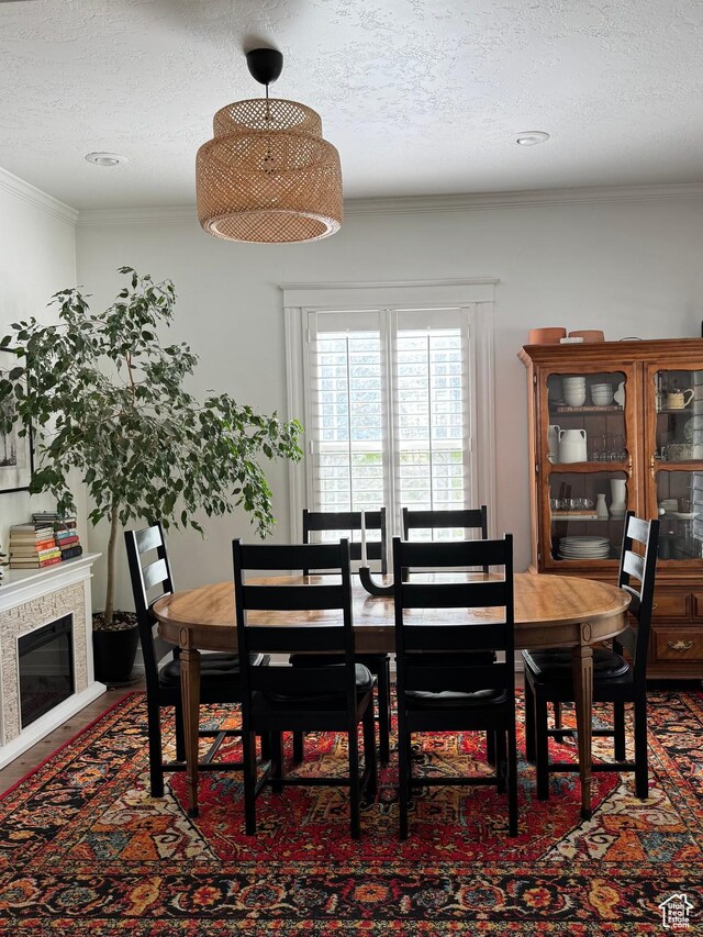 dining space with ornamental molding, a textured ceiling, and a glass covered fireplace