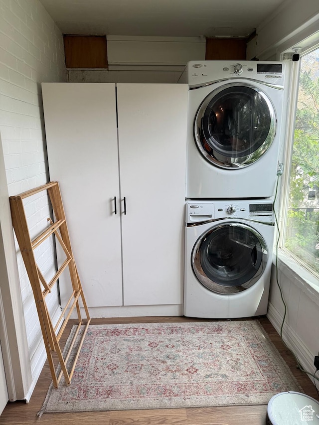 clothes washing area with estacked washer and dryer and wood finished floors