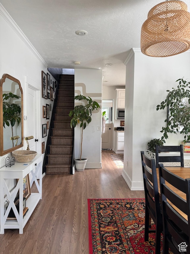 hallway featuring wood finished floors, stairs, a textured ceiling, ornamental molding, and baseboards