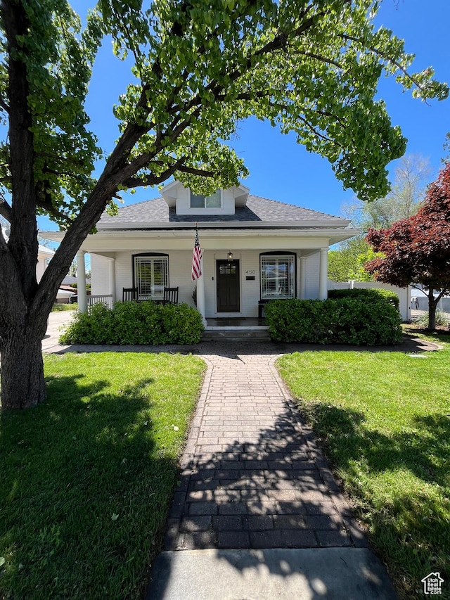 bungalow-style home featuring a porch, a front yard, an attached garage, and roof with shingles