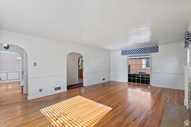 unfurnished living room with arched walkways, wood finished floors, and ornamental molding