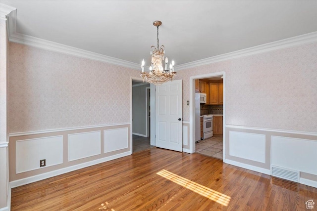 unfurnished dining area featuring a chandelier, light wood finished floors, a wainscoted wall, crown molding, and a decorative wall
