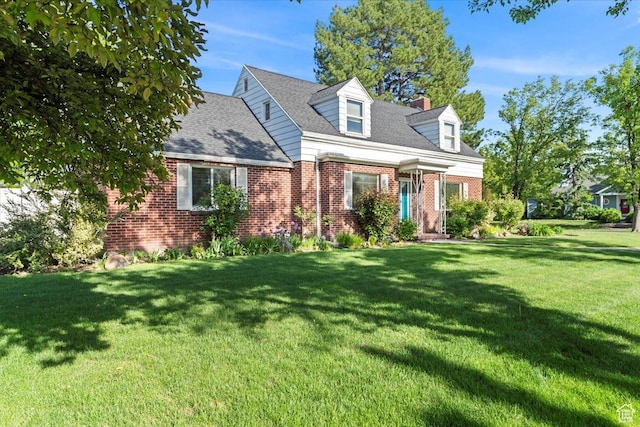 cape cod-style house featuring brick siding, a front yard, and a chimney