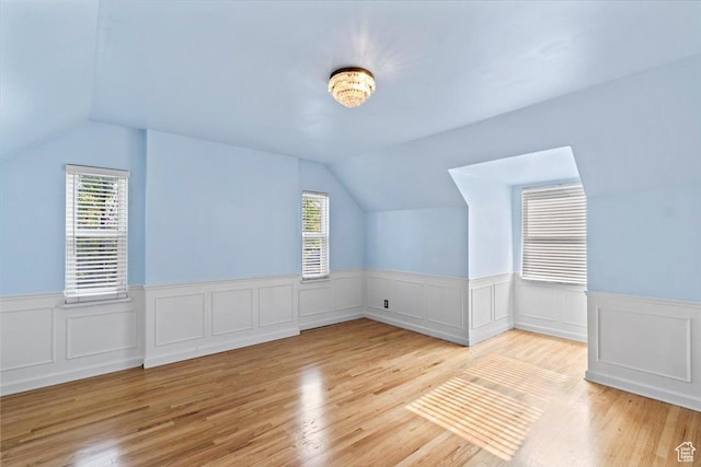 bonus room featuring vaulted ceiling, wainscoting, healthy amount of natural light, and wood finished floors