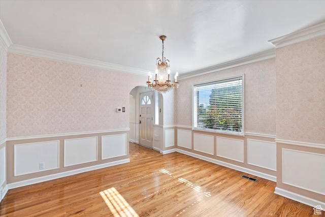 unfurnished dining area with crown molding, arched walkways, a chandelier, wainscoting, and wood finished floors