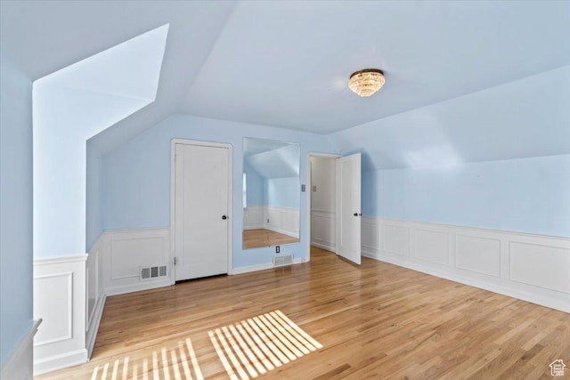bonus room with vaulted ceiling, a wainscoted wall, wood finished floors, and a decorative wall