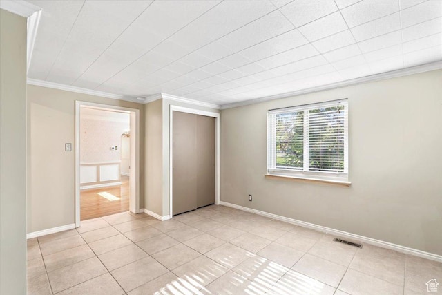 unfurnished bedroom with ornamental molding, light tile patterned flooring, a closet, and baseboards