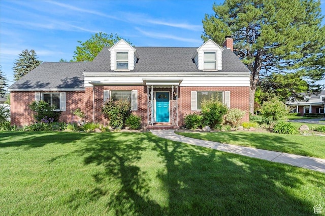 new england style home featuring a chimney, brick siding, and a front lawn