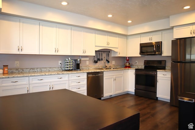 kitchen with appliances with stainless steel finishes, a sink, dark wood finished floors, white cabinets, and recessed lighting
