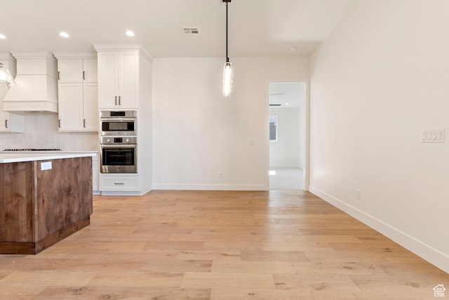 4845 W 2020 S, Hurricane, UT 84737 - kitchen with premium range hood, white cabinets, baseboards, hanging light fixtures, and light wood-type flooring