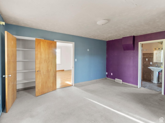 10045 W 12000 N, Bothwell, UT 84337 - unfurnished bedroom featuring a sink, baseboards, connected bathroom, a textured ceiling, and a walk in closet