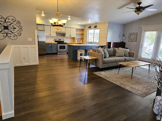 living area featuring healthy amount of natural light, dark wood-type flooring, lofted ceiling, ceiling fan, and a wainscoted wall