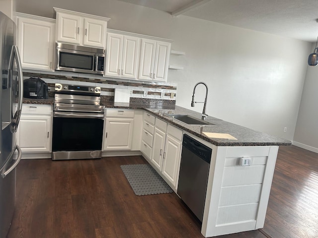 kitchen with stainless steel appliances, a sink, a peninsula, open shelves, and dark countertops