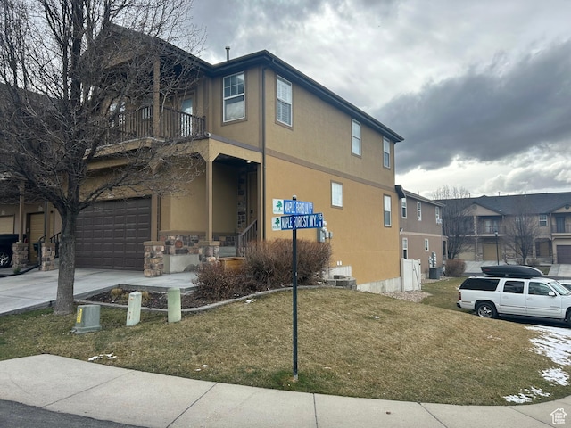 view of home's exterior featuring an attached garage, a balcony, stucco siding, concrete driveway, and a lawn