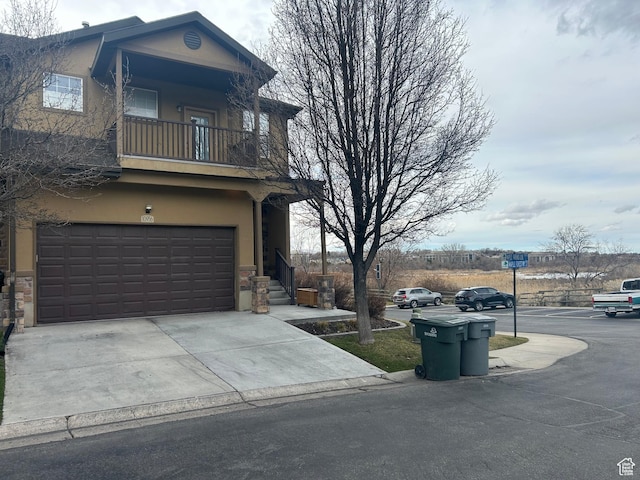 view of side of property with a balcony, stucco siding, a garage, and concrete driveway