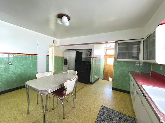 kitchen with wainscoting, a sink, white cabinetry, glass insert cabinets, and dark countertops