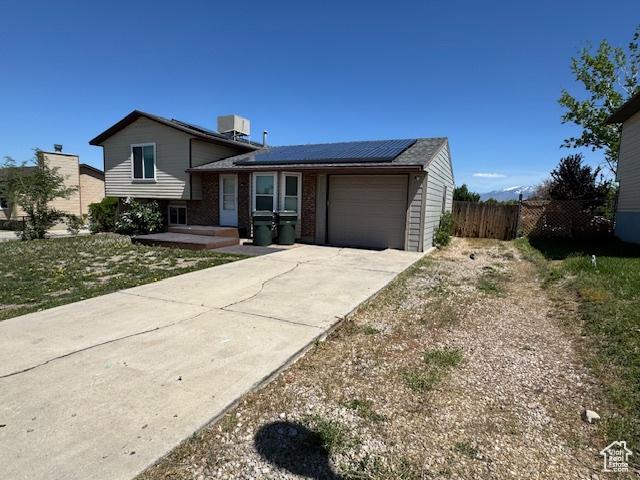 split level home with a garage, fence, driveway, roof mounted solar panels, and central AC unit