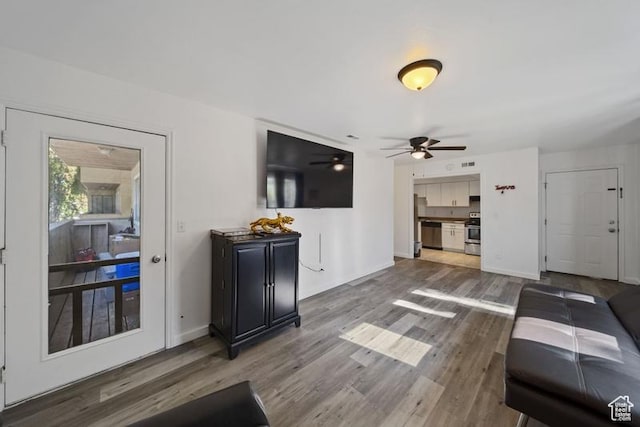 living area featuring wood finished floors, a ceiling fan, and baseboards