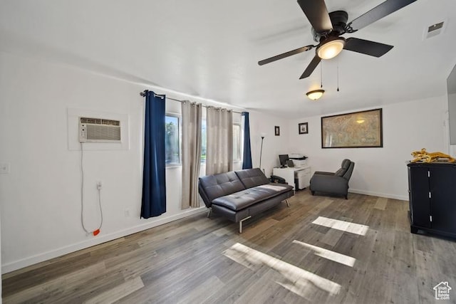 living area featuring wood finished floors, a wall unit AC, a ceiling fan, and baseboards