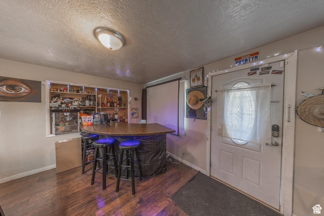 entrance foyer with a bar, a textured ceiling, wood finished floors, and baseboards