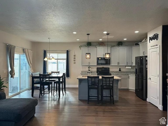 kitchen featuring black appliances, a textured ceiling, dark wood-style floors, a kitchen breakfast bar, and a center island with sink