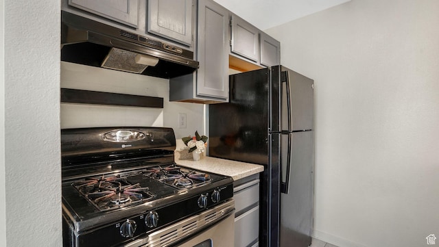 kitchen with range with gas stovetop, under cabinet range hood, freestanding refrigerator, and light countertops