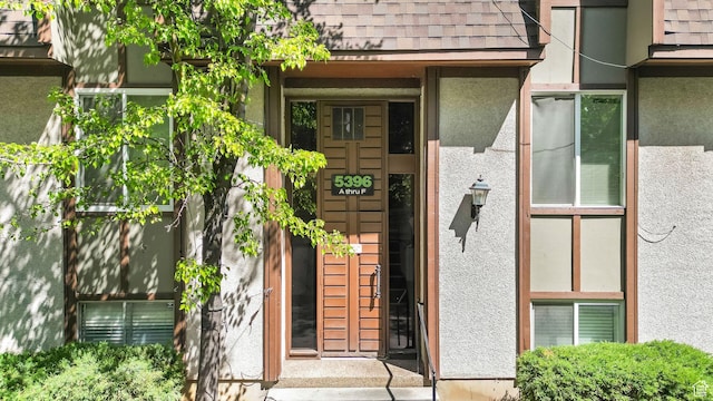 view of exterior entry featuring stucco siding and roof with shingles