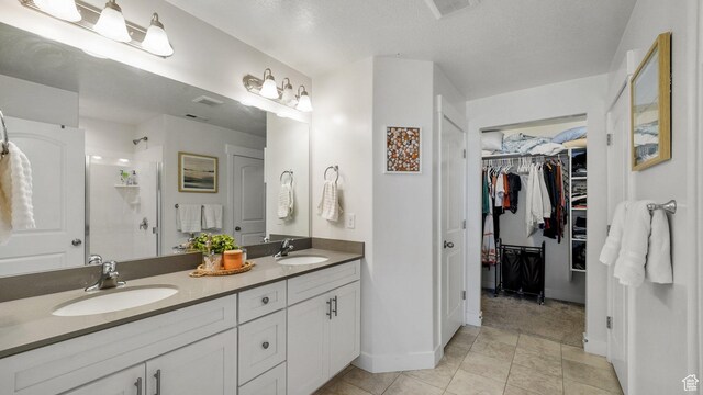 bathroom featuring walk in shower, double vanity, baseboards, a walk in closet, and tile patterned floors