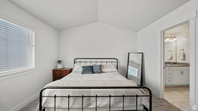 bedroom with a sink, multiple windows, vaulted ceiling, light tile patterned floors, and ensuite bath