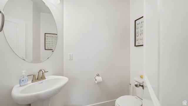 half bath with baseboards, a sink, and toilet
